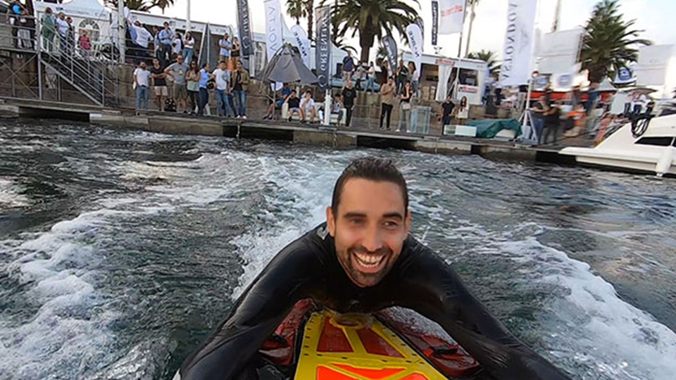 A person in water on a board. There are onlookers in the background. 
